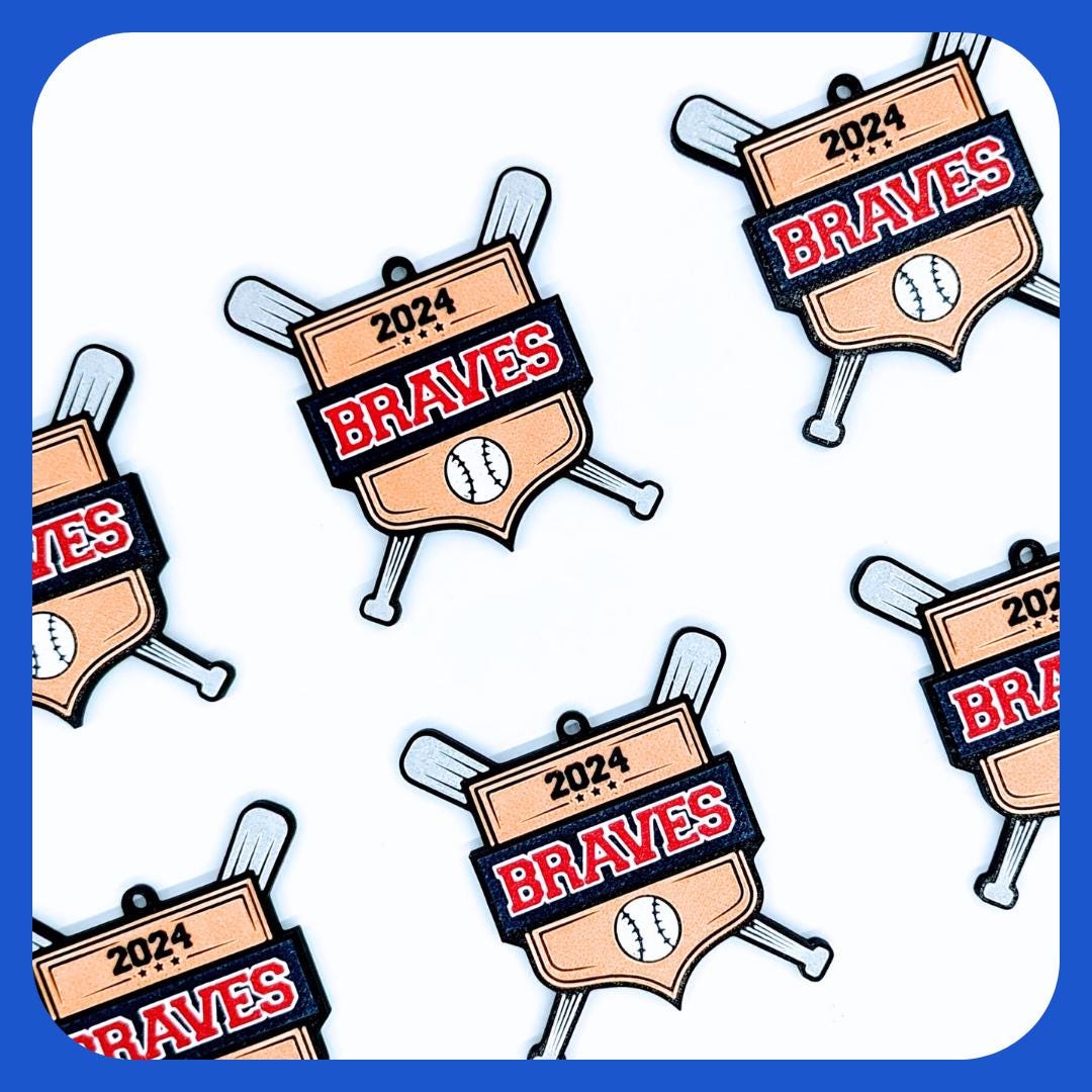 Multiple custom baseball medals featuring a gold shield design with two crossed silver bats. The medals display the team name in bold red and white letters on a black banner, with a baseball icon below. Team gift